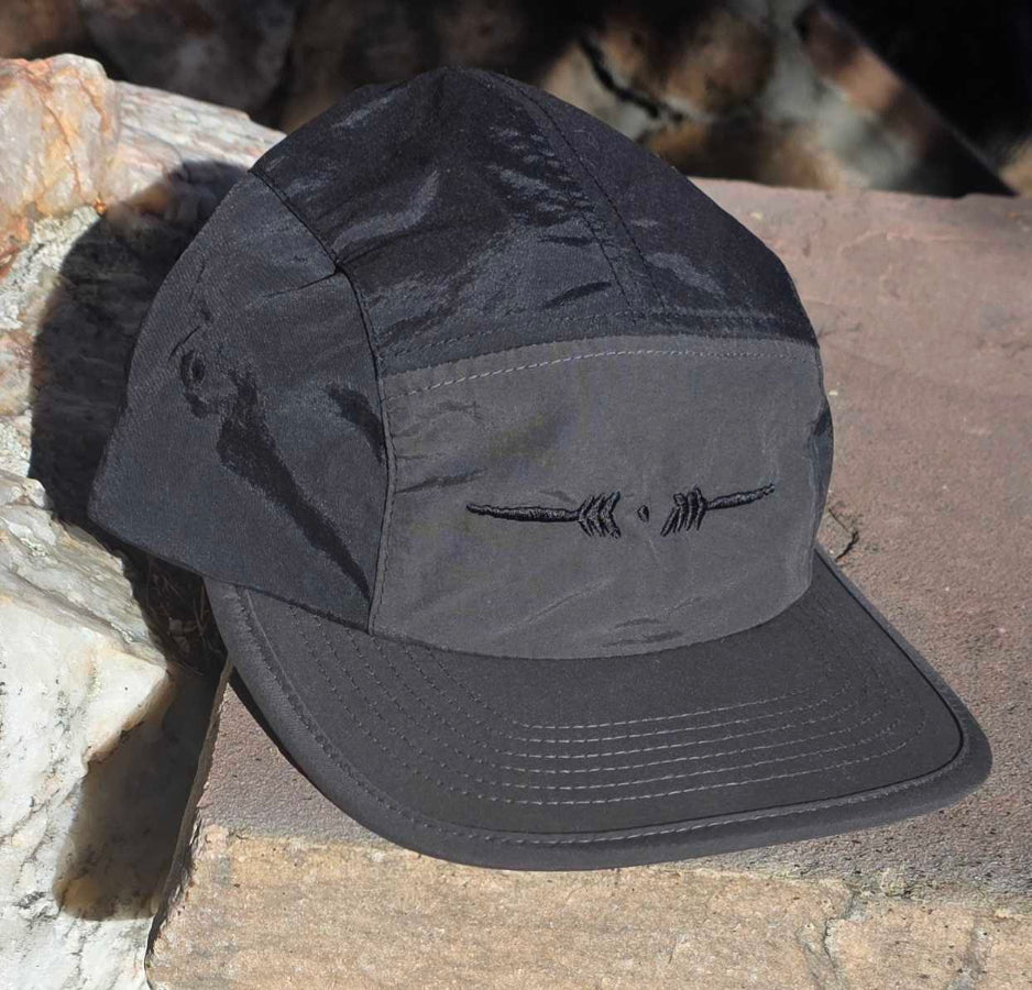 Black and grey cap with a Lost Tribe arrow logo on a stone surface